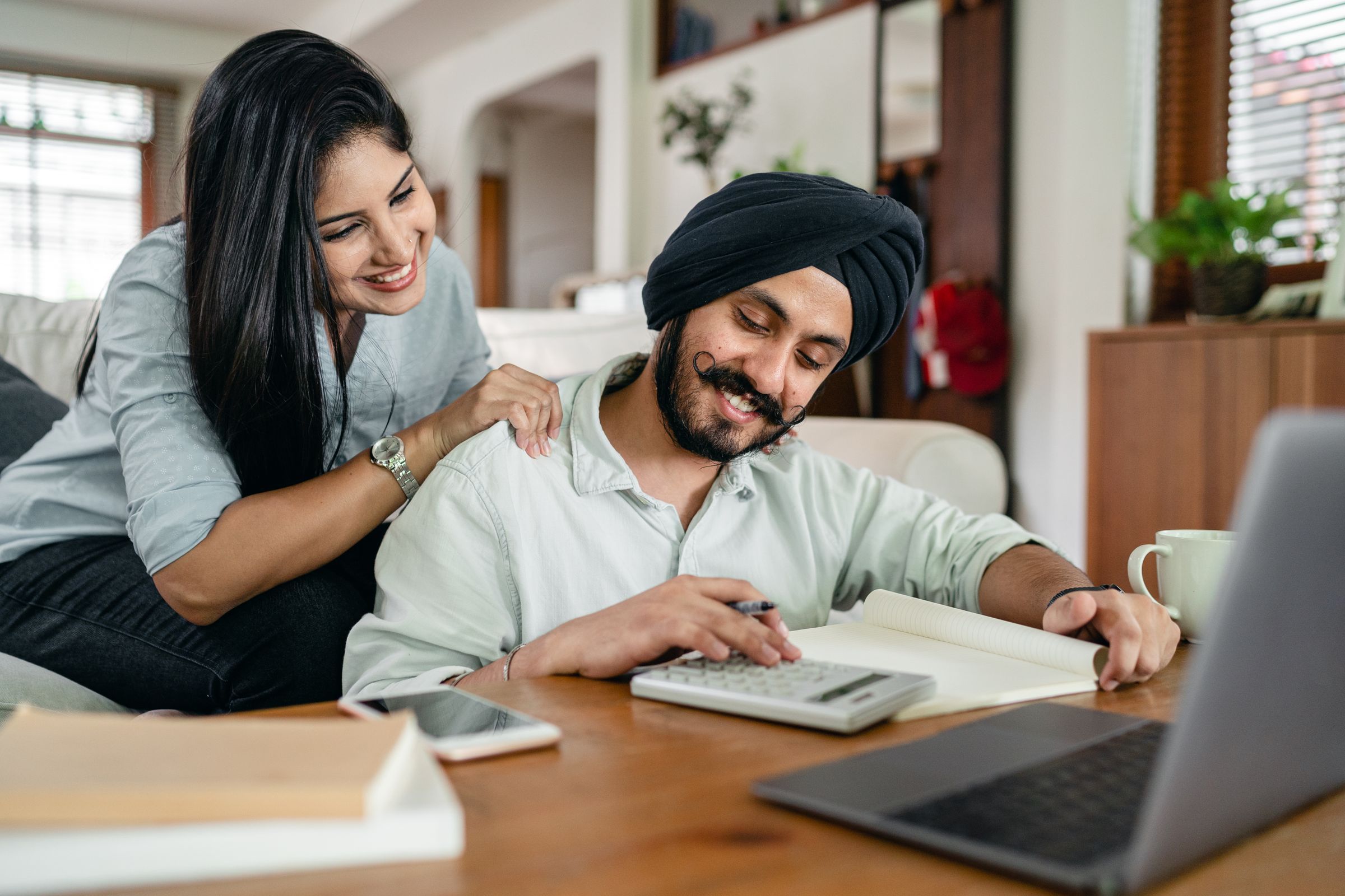A young couple planning their household finances at a table with a laptop and calculator
