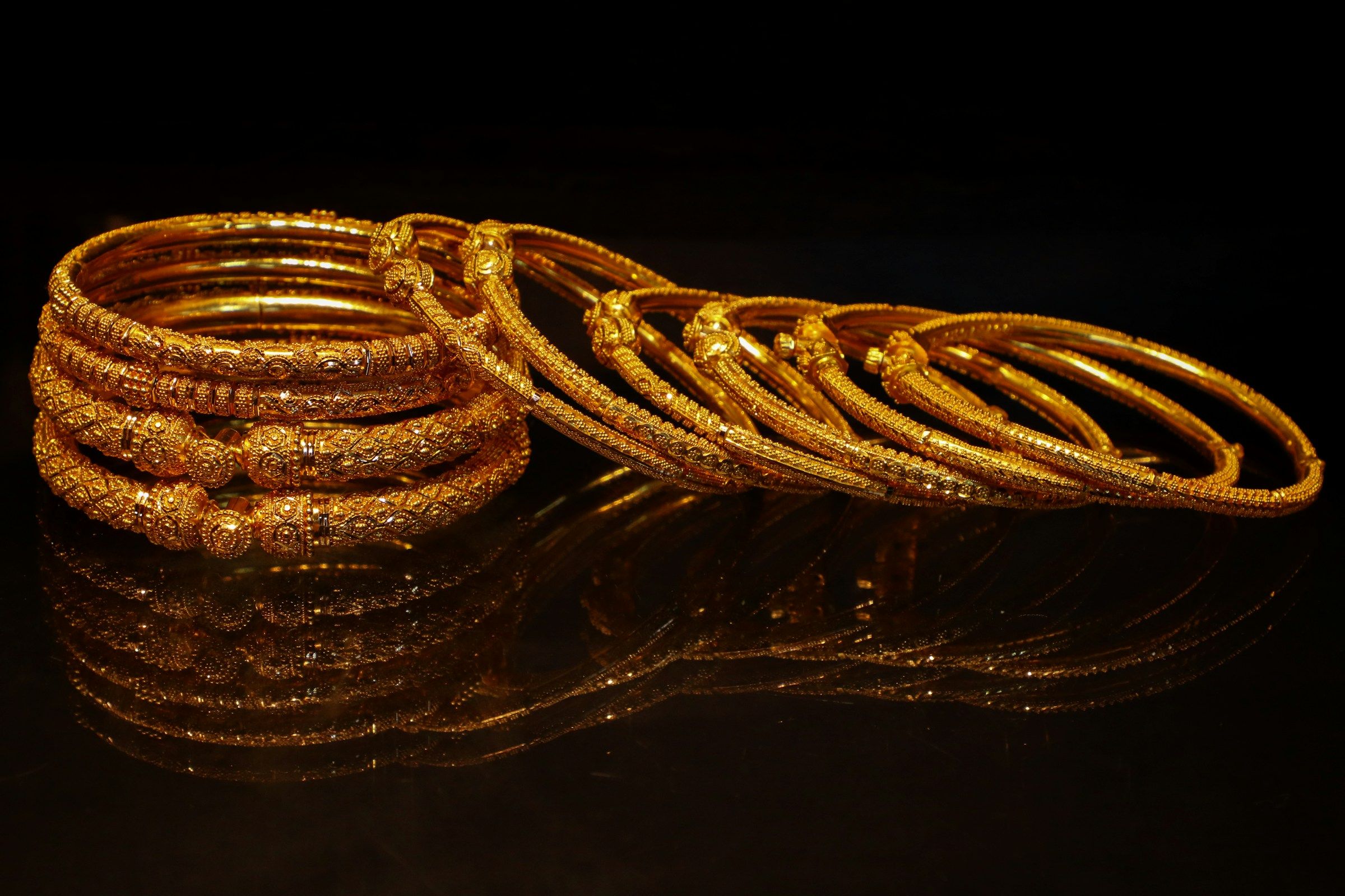 A stack of ornate Indian gold bangles on a reflective black surface