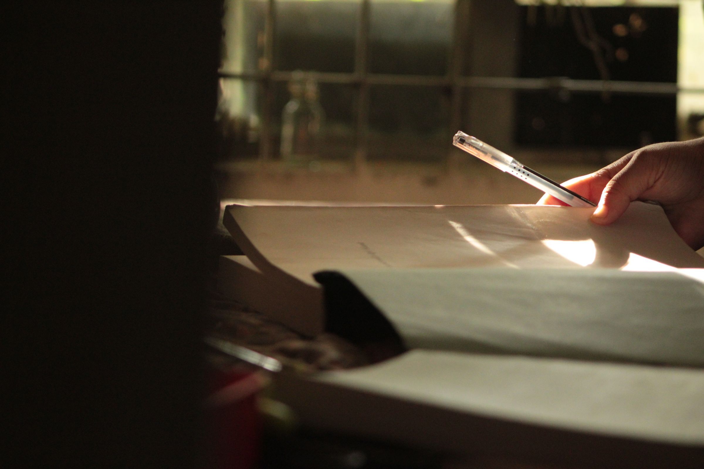 A hand writing in an open notebook beside a window in warm light